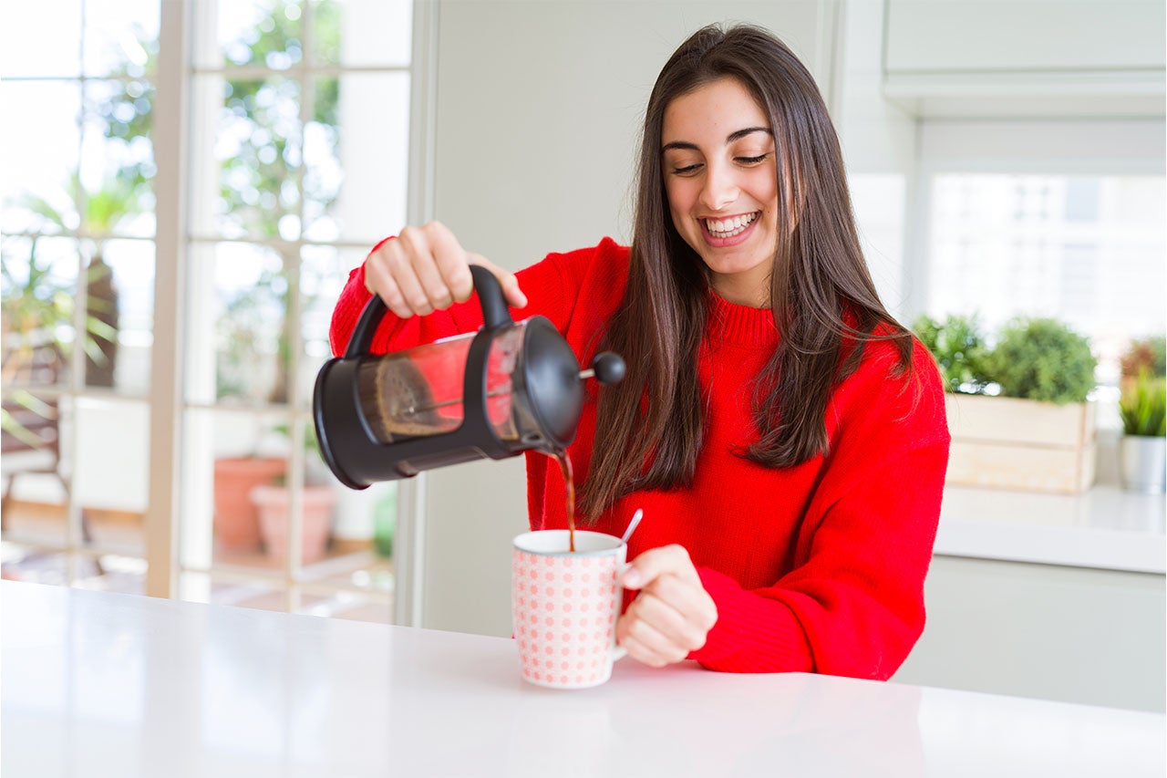 Mulher na cozinha usando uma prensa francesa para preparar o seu café gelado